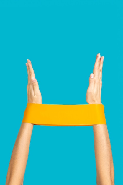 Isolated hands of caucasian woman doing exercises with\
resistance band on turquoise background doing physical activities\
to keep feet getting fit at home by yourself