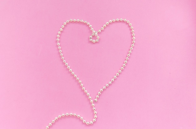 Isolated heart-shaped silver bead necklace on pink background top view, Valentine's day, lovers ' day