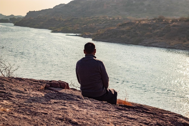 Photo isolated man sitting at mountain top with lake view backbit shot from flat angle