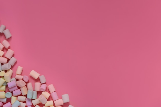 Isolated multicolored marshmallows scattered in the corner on a pink background