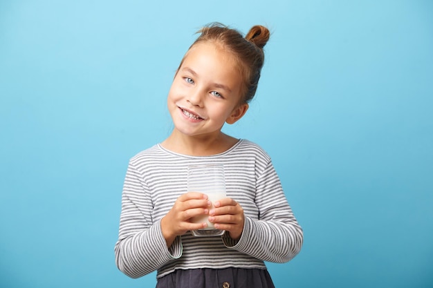 Isolated portrait of funny child girl with glass of milk stands over blue background