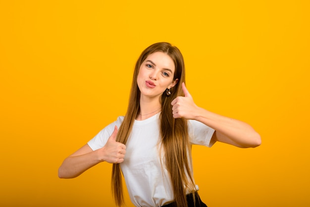 Isolated portrait of happy woman has toothy smile, closes eyes, feels pleasure from compliment, stands over yellow wall. Positive emotions and feelings concept