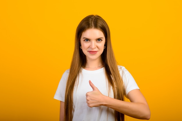 Isolated portrait of happy woman has toothy smile, closes eyes, feels pleasure from compliment, stands over yellow wall. Positive emotions and feelings concept