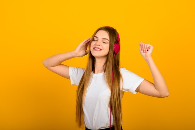 Isolated portrait of happy woman has toothy smile, closes eyes, feels pleasure from compliment, stands over yellow wall.