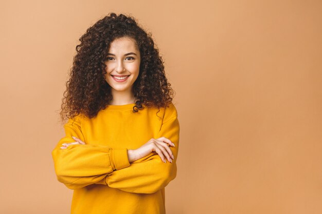 Ritratto isolato della donna sorridente dello studente riccio con le armi attraversate.