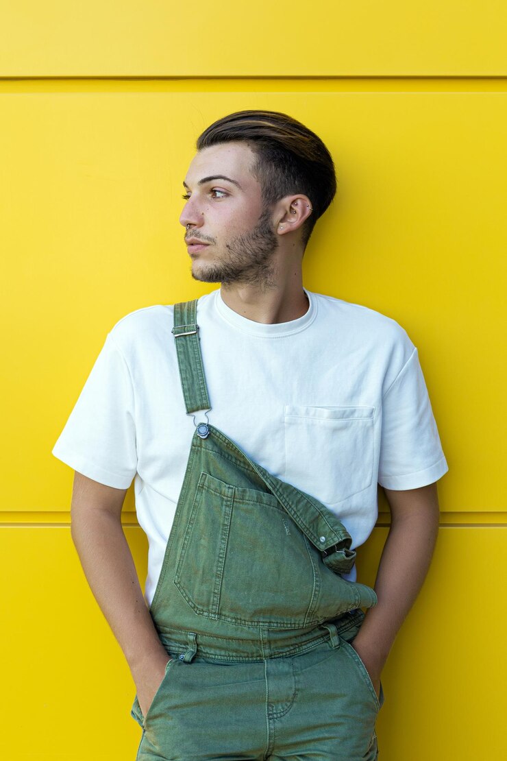 Photo isolated portrait of a young modern man wearing a green overall and white tshirt in front of a yellow wall