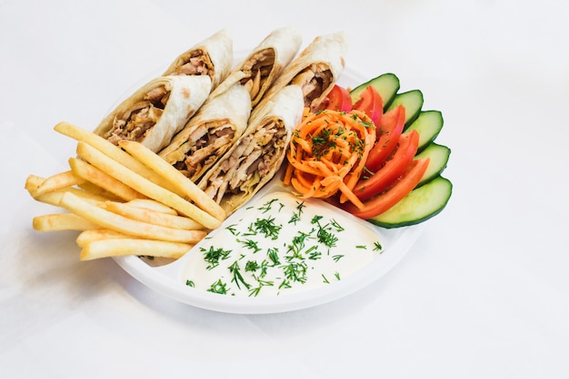 Isolated shawarma in a plate with shadow. Oriental food made from chicken meat, tomatoes, Korean carrots, french fries, cucumbers in pita bread