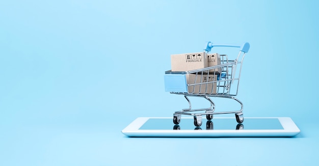 Isolated of Shipping paper boxes inside blue shopping cart trolley on tablet isolated on blue