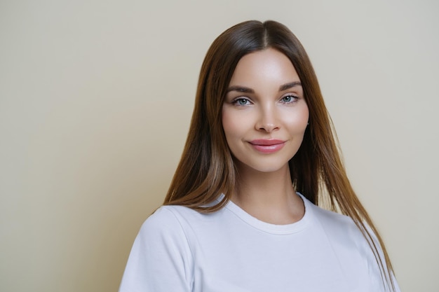 Isolated shot of pleasant looking woman with dark straight hair wears white t shirt isolated over brown background copy space for your advertising content listens interesting stories and good news