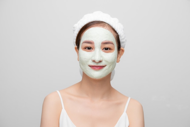 Isolated shot of pretty woman wears facial mask for refreshing skin with her towel over white background.