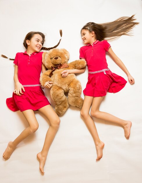 Isolated shot of two smiling girls lying on floor and holding teddy bear