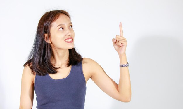 Isolated studio cutout shot of Asian young female model in crop top shirt and jeans standing holding hand pointing finger on blank space showing presenting product advertisement on white background.