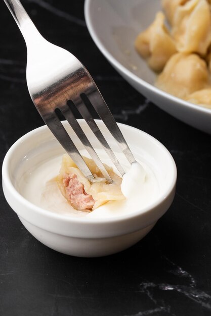 Isolated traditional russian pelmeni ravioli dumplings with meat dipping in sour cream on black background Menu or cook book concept