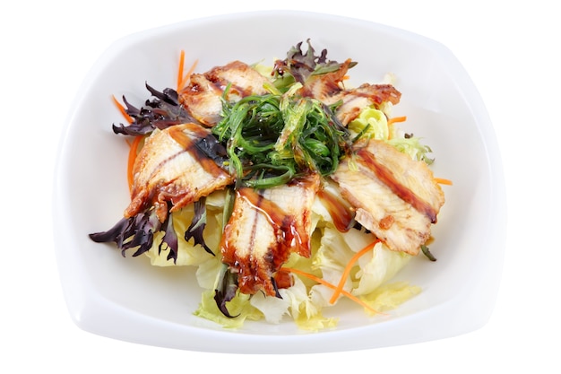 Isolated on white deep bowl with slices of smoked eel, lying on leaves of fresh salad, decorated with seaweed Chuka.