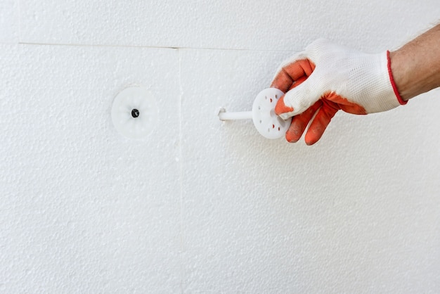 Isolatie van het huis met polyfoam. De arbeider bevestigt een polystyreen bord met plastic pluggen.