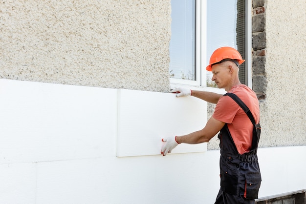 Isolatie van het huis met polyfoam. De arbeider plaatst een piepschuimplaat op de gevel.