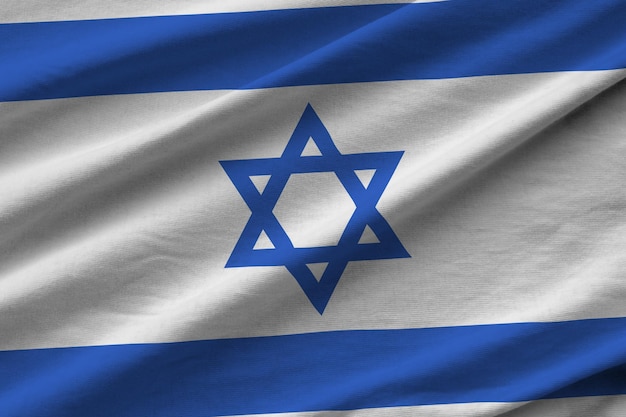 Israel flag with big folds waving close up under the studio light indoors The official symbols and colors in banner