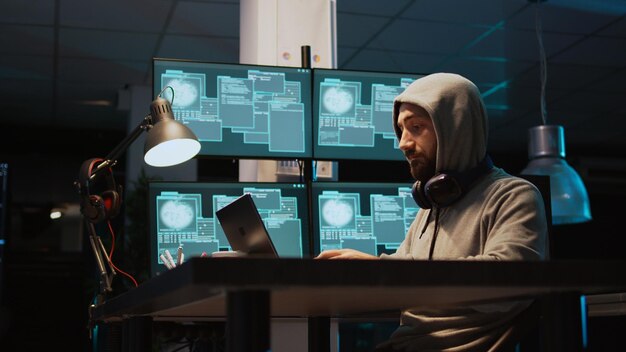 IT-crimineel hacksysteem 's nachts met behulp van een virus om computermalware en serverfouten te produceren. Gegevenshacker steelt informatie van software-app, werkt met meerdere monitoren. Schot uit de hand.