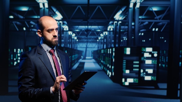 IT engineer using tablet in high tech server room, planning networking computer system. Database admin activating hardware server in data center, mainframe computer processor storage.