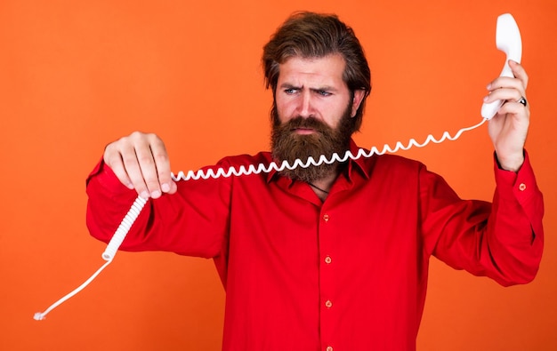 Это сломанный брутальный мужчина с телефонной связью, бородатый мужчина, одетый в красную рубашку, случайный мужчина, отвечающий на звонок, концепция разговора, секретарь или помощник говорят по ретро-телефону