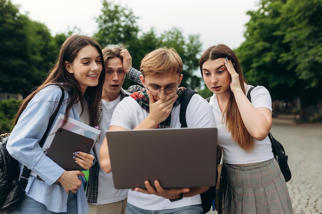 Фото Невероятно удивленная группа студентов смотрит на ноутбук и держит рот открытым, стоя в парке