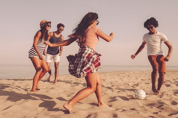 それは私のものです！海を背景にビーチでサッカーボールで遊ぶ陽気な若者のグループ