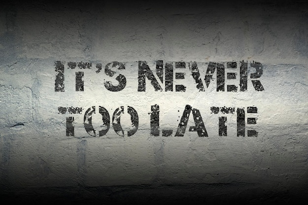 It is never too late stencil print on the grunge white brick wall