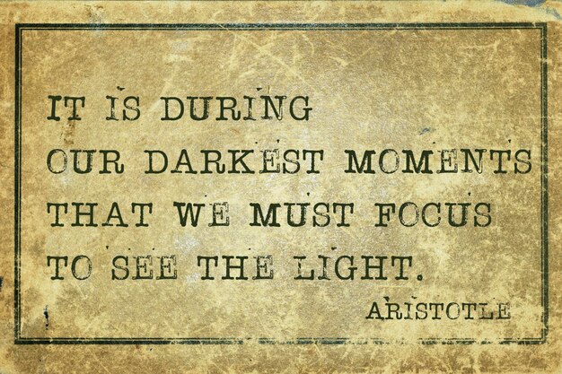 It is during our darkest moments  - ancient Greek philosopher Aristotle quote printed on grunge vintage cardboard