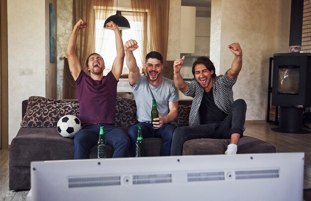 It's a goal. Excited three friends watching soccer on TV at home together.