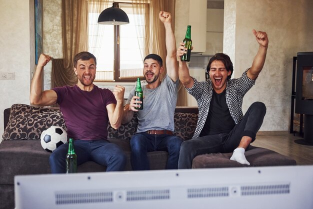 Photo it's a goal. excited three friends watching soccer on tv at home together.