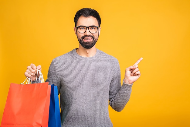 It's shopping time! happy bearded happy young man with colorful paper bags isolated over yellow background. pointing finger