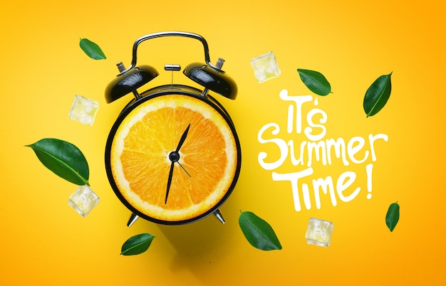 It's Summer Time Typography. Alarm Clock of Orange Fruit Green Leaves and Ice Cube Flying 