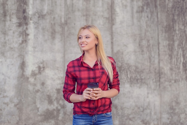 It's time for takeaway coffee! Young smiling girl enjoying coffee for breakfast. She is dressed in red checkered shirt and jeans