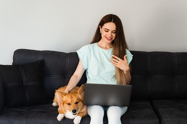 ラップトップを持つ IT スペシャリストの女の子と同僚とオンラインでコーギー犬のチャット 身振りで示し、新しいプロジェクトの創造的な概念を説明します 自宅でのウェルシュ・コーギー・ペンブロークとのチームワーク