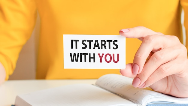 It starts with you is written on a white business card. A woman's hand holds a white paper card. 