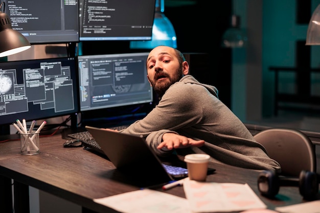 Foto ingegnere di sistema it che codifica il database su più monitor per programmare la nuova interfaccia del server di notte. lavora fuori orario per sviluppare il codice sorgente html sulla finestra del terminale, intelligenza artificiale.