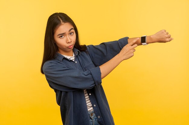 It39s laat opschieten portret van ontevreden drukke vrouw in denim shirt kijken ongeduldig en wijzend polshorloge waarschuwing van deadline tijd om te gaan indoor studio shot geïsoleerd op gele achtergrond