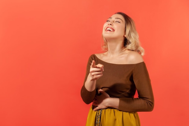 It39s really you Portrait of a young woman standing and laughing out loud wondering and pointing finger at the camera Excited reaction to the joke Indoor studio shot isolated on red background