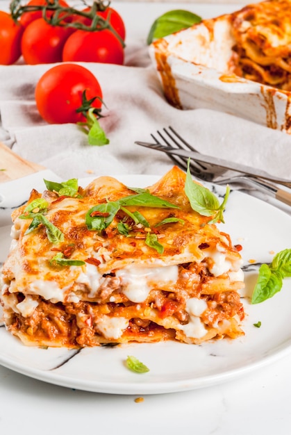 Foto italiaans eten recept. diner met klassieke lasagne bolognese met bechamelsaus, parmezaanse kaas, basilicum en tomaten, op een witte marmeren tafel, coopy ruimte