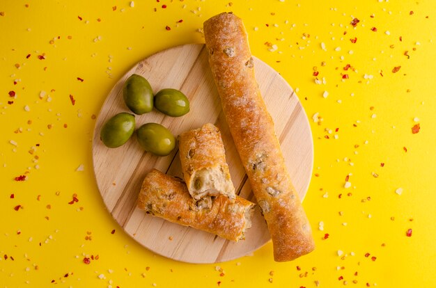 Italiaans olijfbrood op houten scherpe raad op gele achtergrond