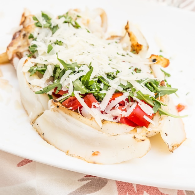 Italiaans restaurant in Gallipoli, regio Puglia (Zuid-Italië). Traditionele inktvis met frisse salade, tomaten en echte Parmigiano kaas. Daglicht.