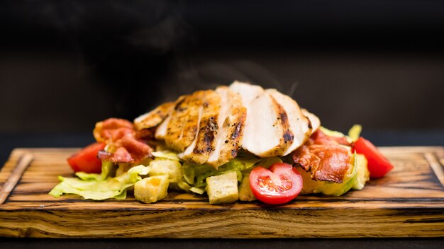 Italiaans restaurantmenu. Close-up van Caesarsalade met gerookte kipfilet, baconchips en groenten op een houten bord.