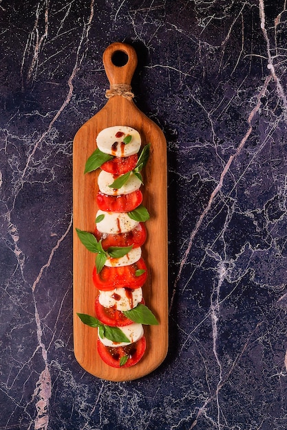 Italiaanse caprese salade met gesneden tomaten, mozzarella, basilicum, olijfolie op een houten serveerplank.