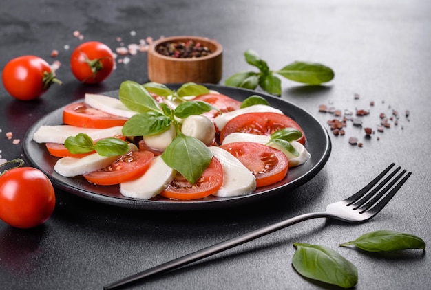 Italiaanse caprese salade met gesneden tomaten, mozzarella kaas, basilicum, olijfolie. Geserveerd in vintage zwarte plaat op een donkere betonnen ondergrond