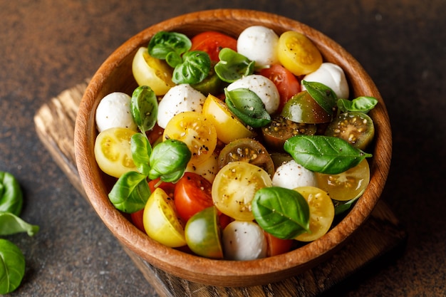 Italiaanse caprese salade met gesneden tomaten, mozzarella kaas, basilicum, olijfolie in houten kom.