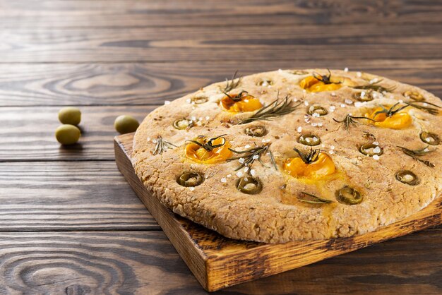 Italiaanse focaccia met olijven, tomaten, rozemarijn en kruiden op een bruine houten tafel