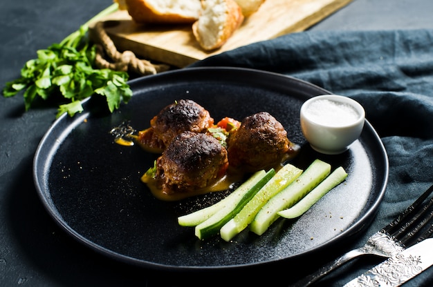 Italiaanse gehaktballen in tomatensaus op een zwarte plaat, komkommers, zout, brood.