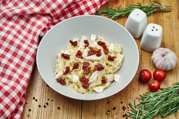 Italiaanse huisgemaakte tagliatelle met gedroogde tomaten, kip en mozzarella in een beige pial op hout.