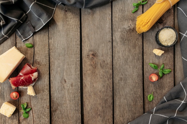 Italiaanse keuken concept plat leggen. Parmezaanse kaasblokjes, geraspte kaas in een zwarte kom, rauwe pasta, dungesneden ham