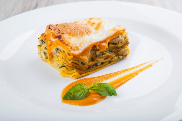 Italiaanse lasagne met vlees op een wit bord met saus en basilicum